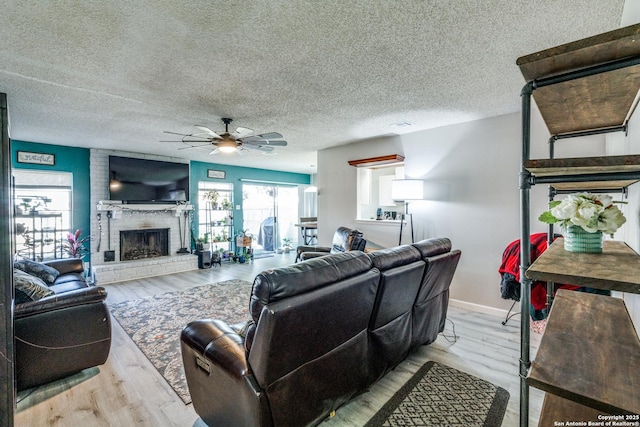 living room featuring light hardwood / wood-style flooring, a textured ceiling, a fireplace, and ceiling fan