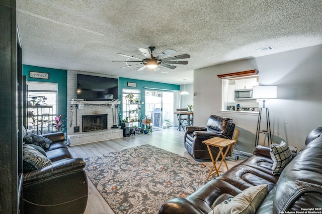 living room featuring a fireplace, a textured ceiling, light hardwood / wood-style flooring, and ceiling fan