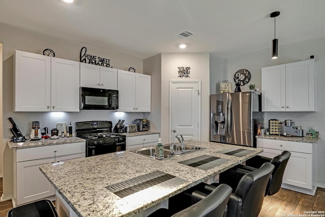 kitchen with a center island with sink, sink, hanging light fixtures, and black appliances