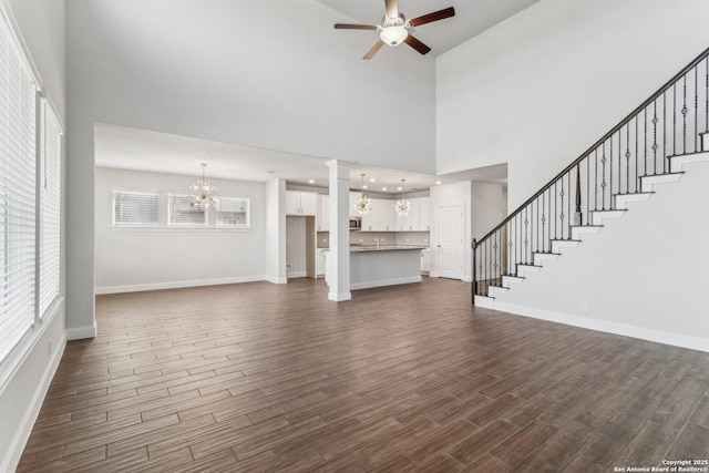 unfurnished living room with a towering ceiling, dark hardwood / wood-style floors, and ceiling fan with notable chandelier