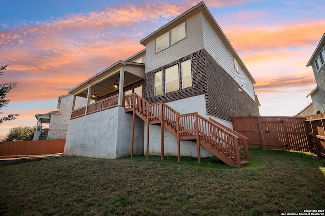 back house at dusk with ceiling fan and a yard