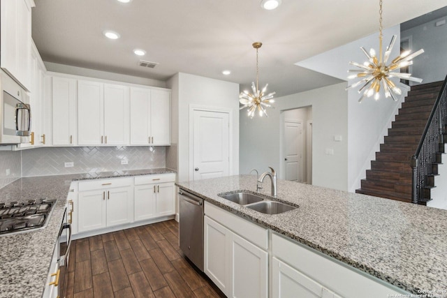 kitchen with appliances with stainless steel finishes, white cabinetry, sink, a chandelier, and light stone countertops