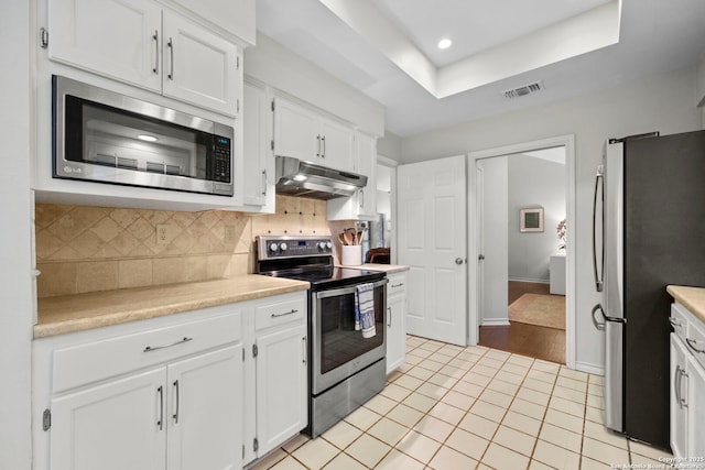 kitchen featuring light tile patterned floors, backsplash, stainless steel appliances, white cabinets, and a raised ceiling