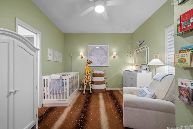 carpeted bedroom with a crib and ceiling fan