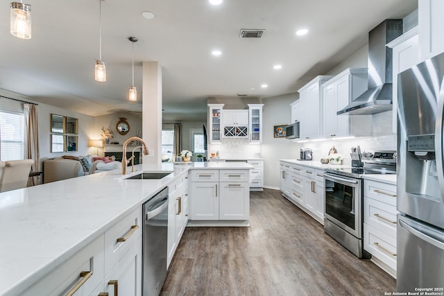 kitchen featuring decorative light fixtures, white cabinetry, sink, stainless steel appliances, and wall chimney range hood