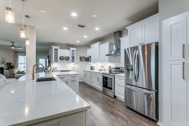 kitchen featuring wall chimney range hood, sink, hanging light fixtures, stainless steel appliances, and white cabinets