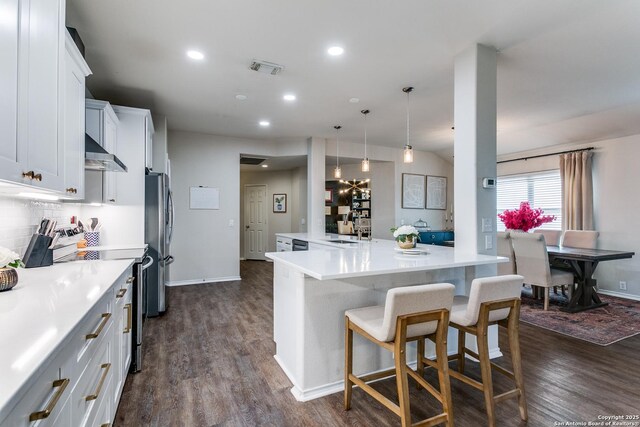 kitchen with decorative light fixtures, white cabinetry, sink, stainless steel fridge, and wall chimney exhaust hood