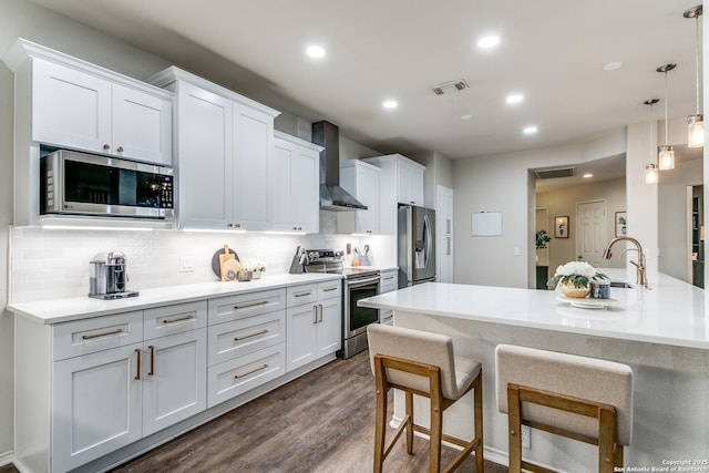 kitchen featuring pendant lighting, wall chimney range hood, stainless steel appliances, and white cabinets