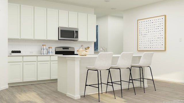 kitchen with stainless steel appliances, tasteful backsplash, light hardwood / wood-style floors, white cabinets, and a kitchen bar