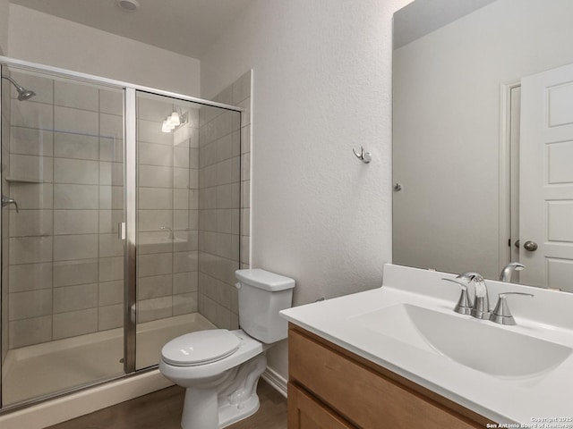 full bath with toilet, vanity, wood finished floors, and a stall shower