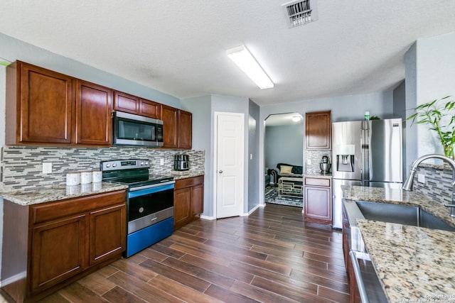 kitchen featuring tasteful backsplash, dark hardwood / wood-style flooring, appliances with stainless steel finishes, and light stone counters