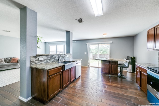 kitchen featuring sink, appliances with stainless steel finishes, a kitchen breakfast bar, light stone countertops, and backsplash