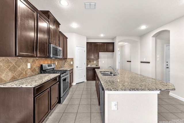 kitchen featuring appliances with stainless steel finishes, sink, backsplash, a kitchen island with sink, and light tile patterned floors