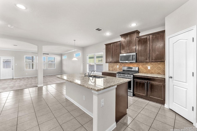 kitchen featuring light tile patterned flooring, sink, stainless steel appliances, light stone countertops, and a center island with sink