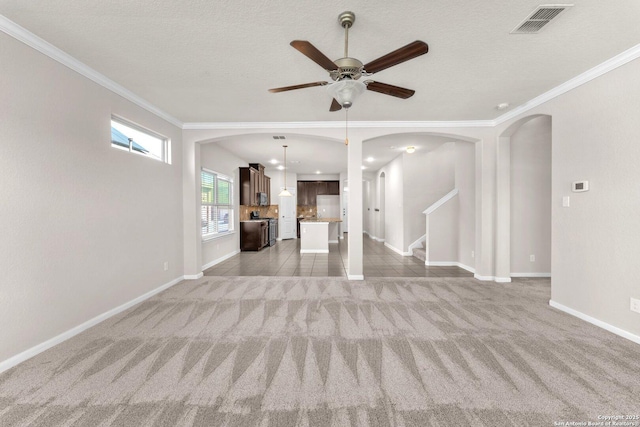 unfurnished living room featuring ceiling fan, crown molding, carpet floors, and a textured ceiling