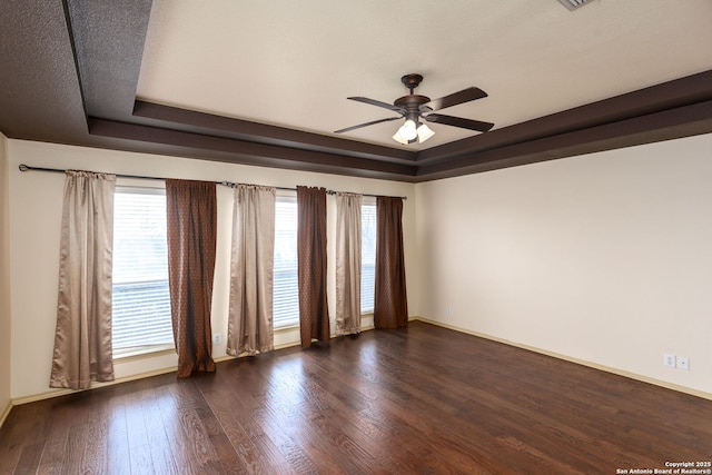 unfurnished room featuring dark wood-type flooring, ceiling fan, and a tray ceiling