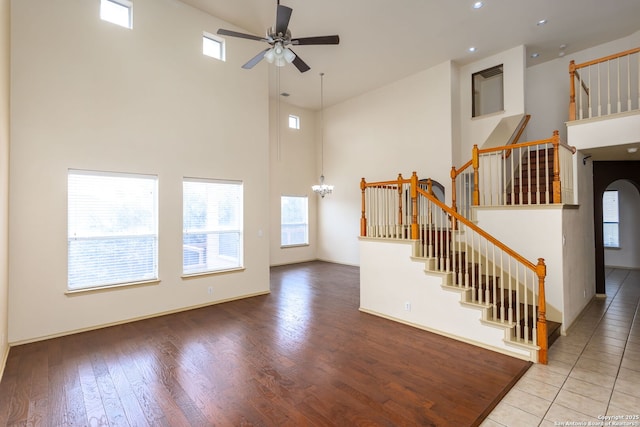 unfurnished living room with wood-type flooring, a towering ceiling, and ceiling fan with notable chandelier