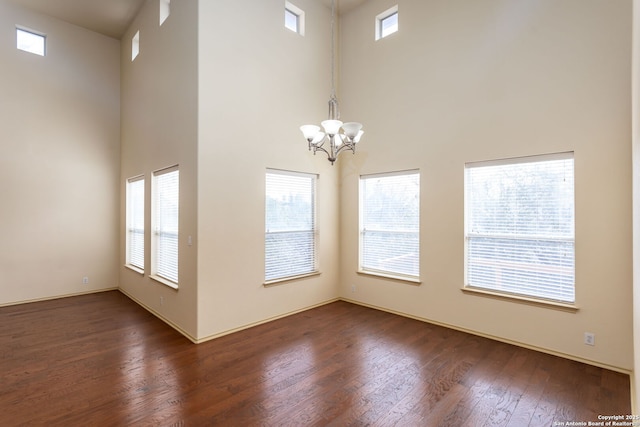 unfurnished room with dark wood-type flooring, an inviting chandelier, and a towering ceiling