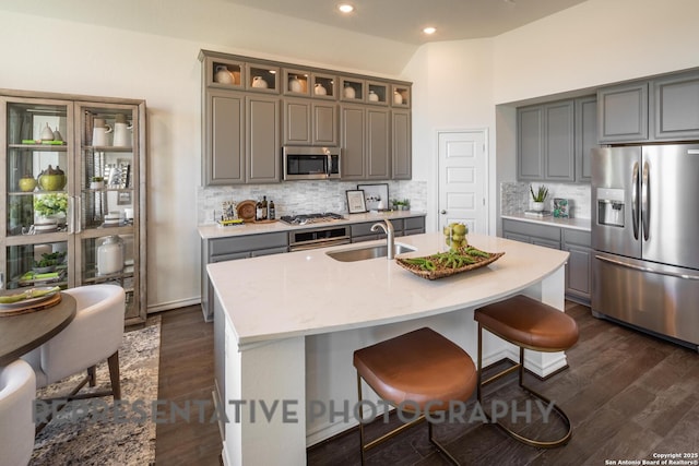 kitchen with sink, appliances with stainless steel finishes, backsplash, dark hardwood / wood-style floors, and an island with sink