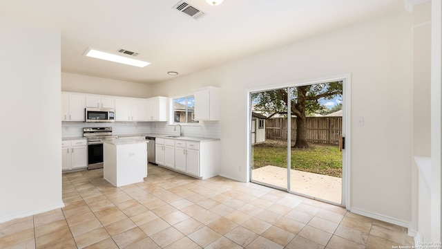 kitchen with decorative backsplash, stainless steel appliances, white cabinets, and a kitchen island