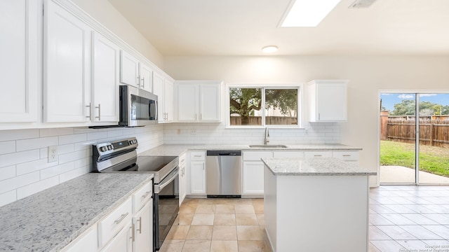 kitchen with sink, white cabinetry, light stone counters, appliances with stainless steel finishes, and backsplash