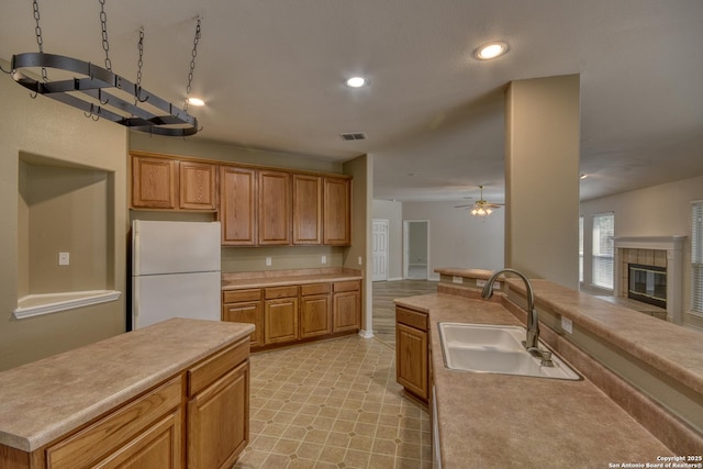 kitchen with white fridge, sink, a center island, a tile fireplace, and ceiling fan