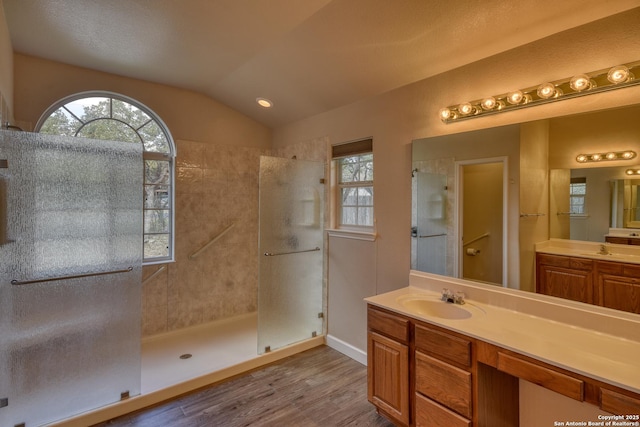 bathroom featuring hardwood / wood-style flooring, lofted ceiling, vanity, and a tile shower