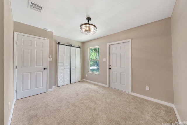 unfurnished bedroom with light colored carpet, a barn door, and a closet