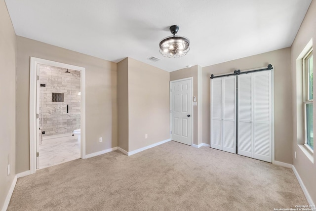 unfurnished bedroom with a closet, ensuite bathroom, and light carpet