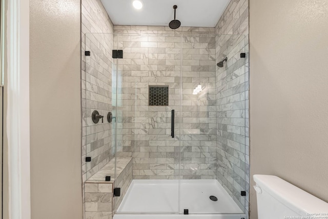 bathroom featuring a shower with door and toilet