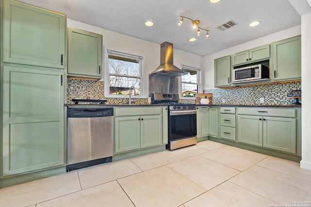 kitchen with light tile patterned flooring, green cabinetry, island range hood, appliances with stainless steel finishes, and backsplash