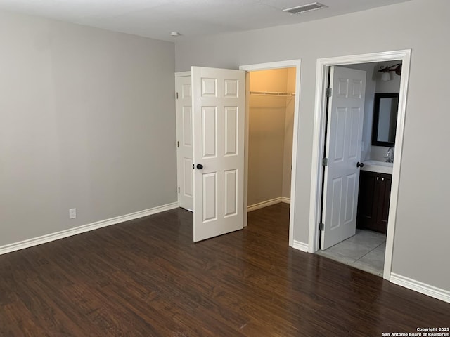 unfurnished bedroom featuring wood-type flooring, a spacious closet, connected bathroom, and a closet