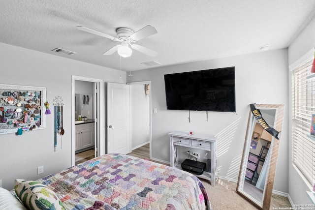 bedroom with ceiling fan, carpet flooring, ensuite bathroom, and a textured ceiling