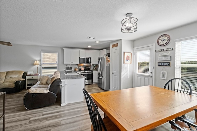 dining area with sink, a notable chandelier, a textured ceiling, and light hardwood / wood-style flooring