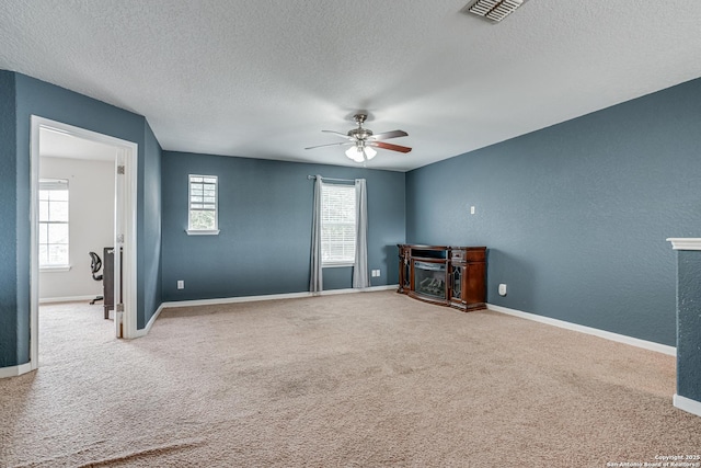 unfurnished living room with ceiling fan, carpet flooring, a fireplace, and a textured ceiling