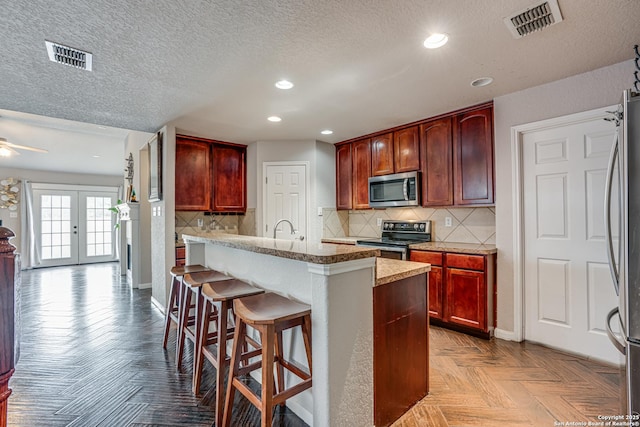 kitchen with tasteful backsplash, a kitchen breakfast bar, stainless steel appliances, light parquet flooring, and french doors