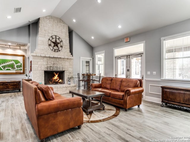 living room featuring a stone fireplace, high vaulted ceiling, light wood-type flooring, and french doors