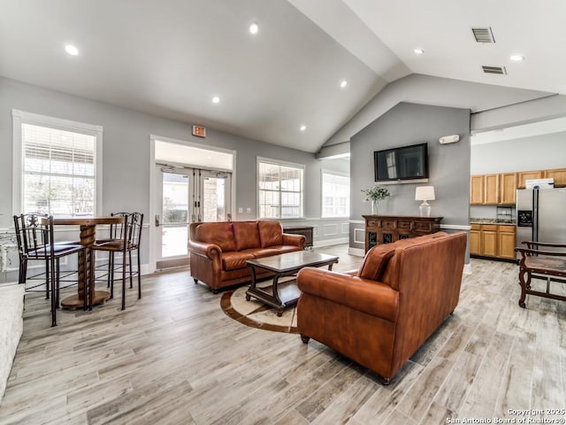 living room featuring french doors, lofted ceiling, and light wood-type flooring