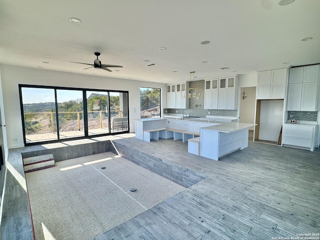 kitchen featuring a spacious island, decorative light fixtures, light hardwood / wood-style floors, decorative backsplash, and white cabinets