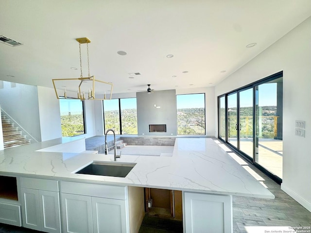 kitchen with decorative light fixtures, light stone countertops, sink, and white cabinets