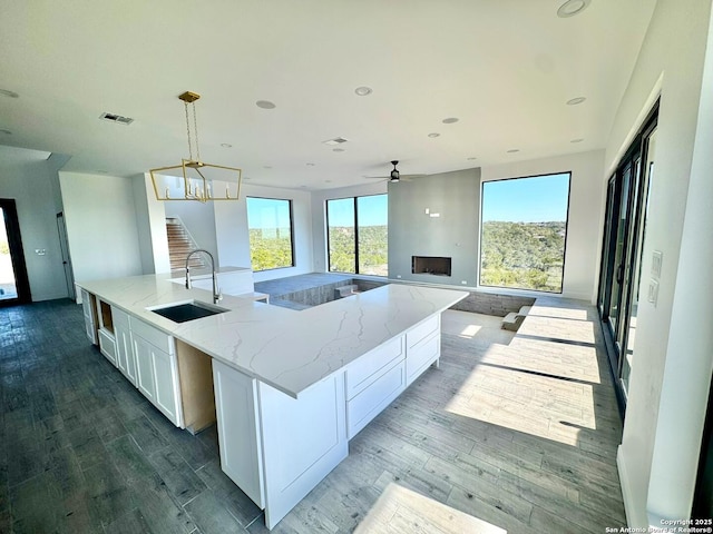 kitchen featuring pendant lighting, white cabinetry, sink, light stone countertops, and a spacious island