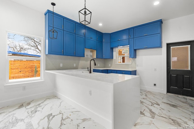 kitchen featuring backsplash, hanging light fixtures, kitchen peninsula, a healthy amount of sunlight, and blue cabinetry