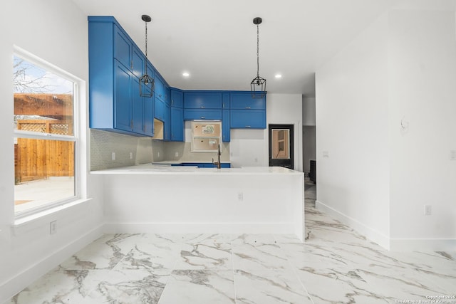 kitchen with blue cabinetry, sink, kitchen peninsula, pendant lighting, and backsplash