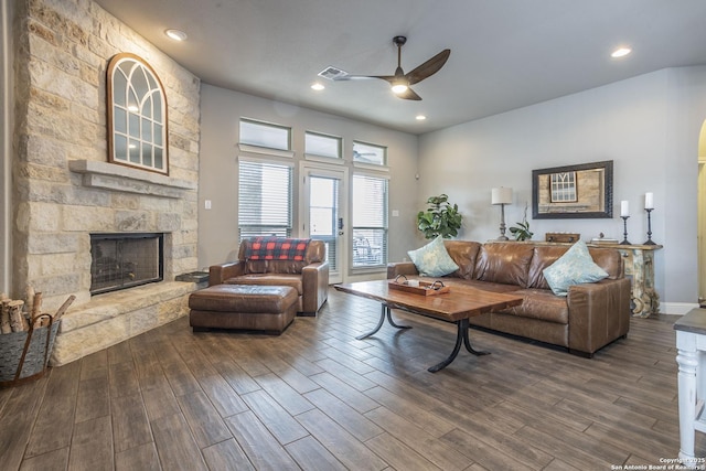 living room with a stone fireplace, dark hardwood / wood-style floors, and ceiling fan