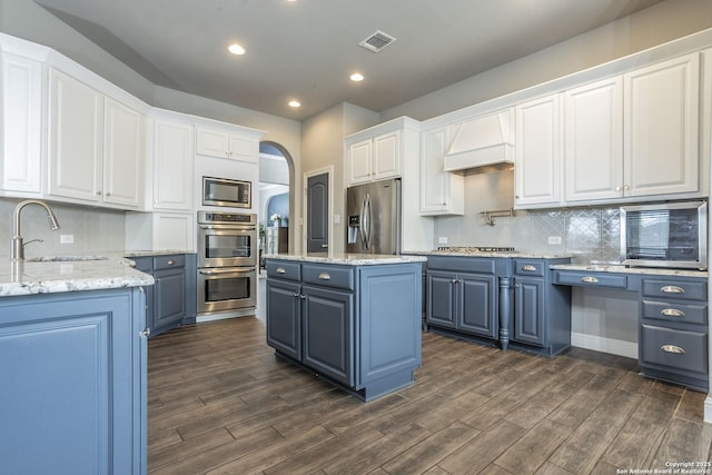 kitchen with a kitchen island, appliances with stainless steel finishes, sink, white cabinets, and custom range hood