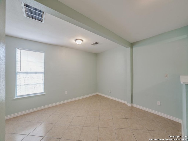 unfurnished room with beam ceiling and light tile patterned flooring