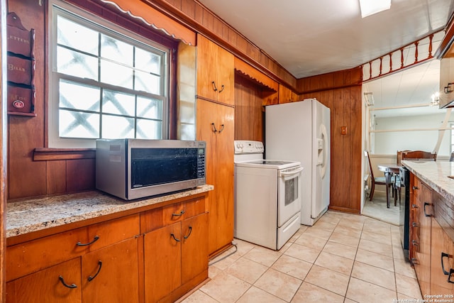 kitchen featuring light stone countertops, wooden walls, light tile patterned floors, and white appliances