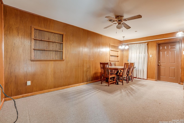 carpeted dining area with wooden walls and ceiling fan with notable chandelier