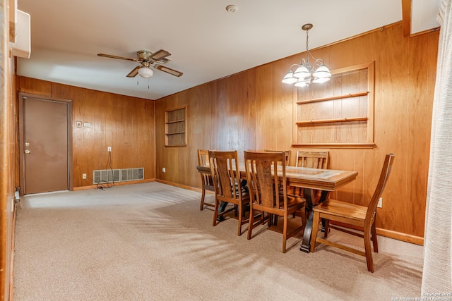 carpeted dining area featuring ceiling fan with notable chandelier and wooden walls