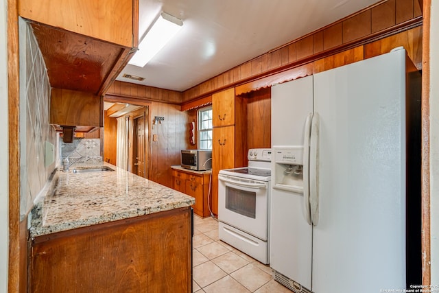 kitchen featuring sink, white appliances, wooden walls, light stone counters, and light tile patterned flooring